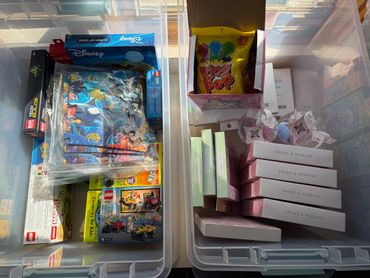 Two storage bins with assorted toys and gift boxes organized inside.