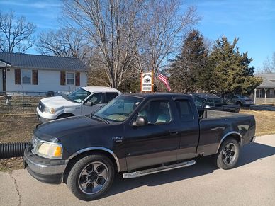Black Ford F-150 truck parked on a sunny street with other vehicles in the background.