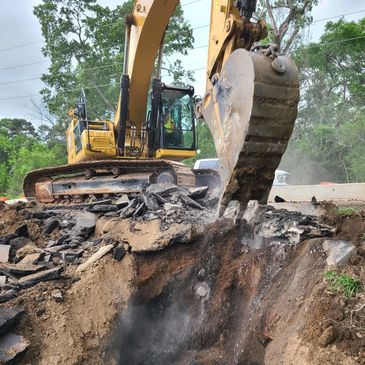 Excavator digging and breaking asphalt on a construction site.