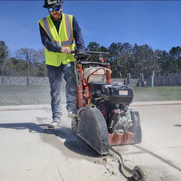 Worker cutting concrete with a large saw on a sunny day.