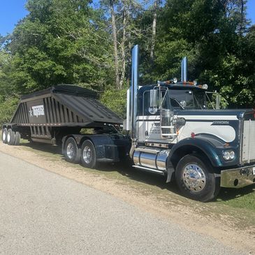 A large semi-truck with a tilted dump trailer parked on a roadside.