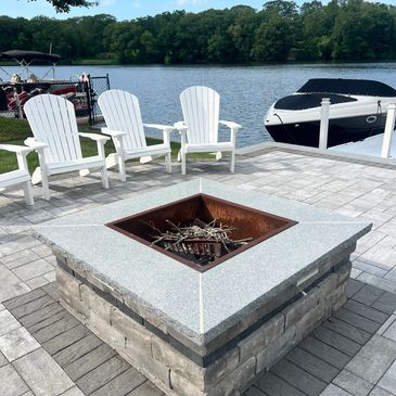 Fire pit with white chairs by a lake and boat dock.