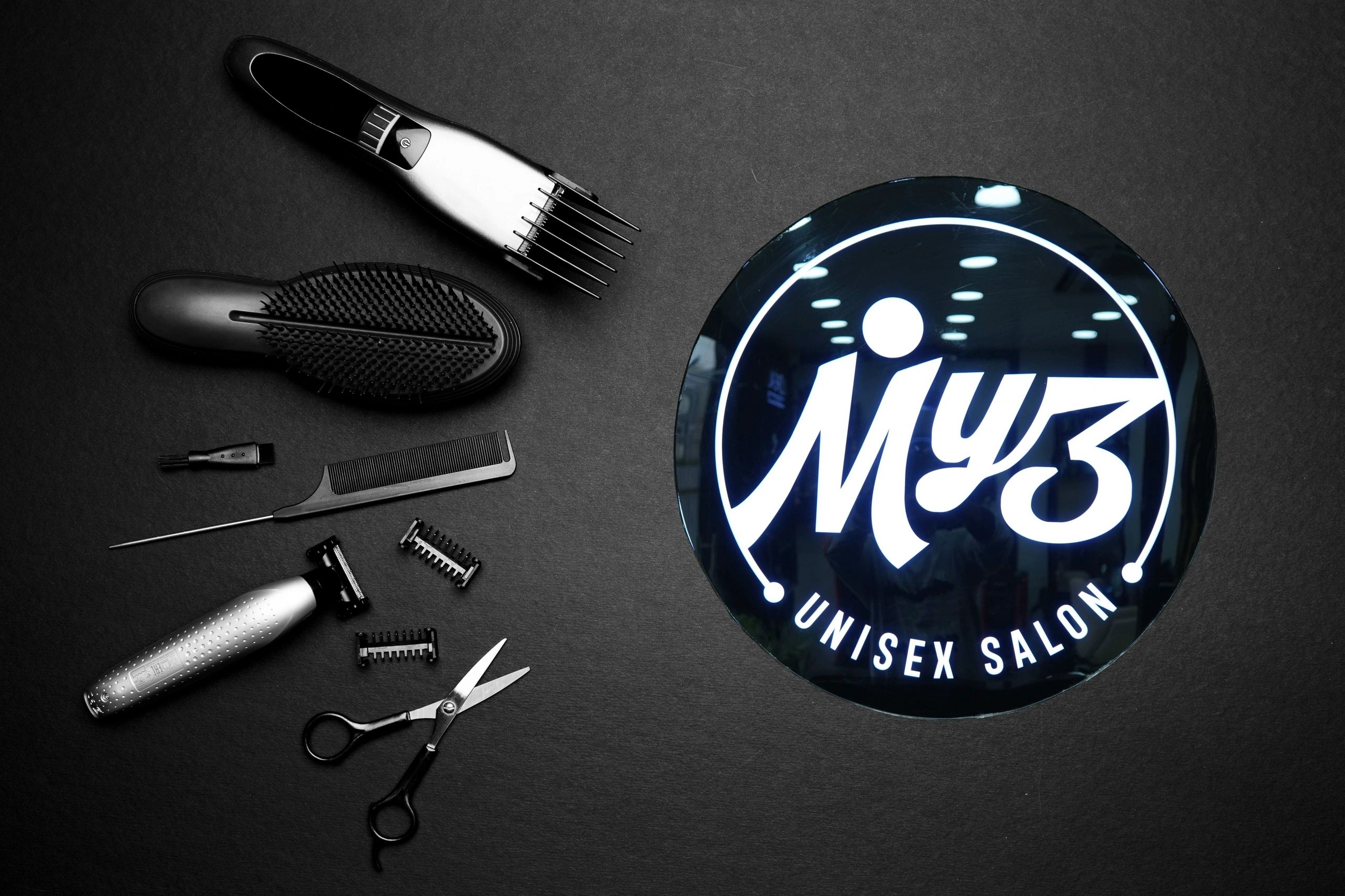 Hairdressing tools and a glowing salon sign on a dark surface.