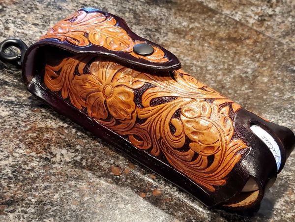 Intricately carved leather golf ball sleeve with western floral designs and a snap closure.