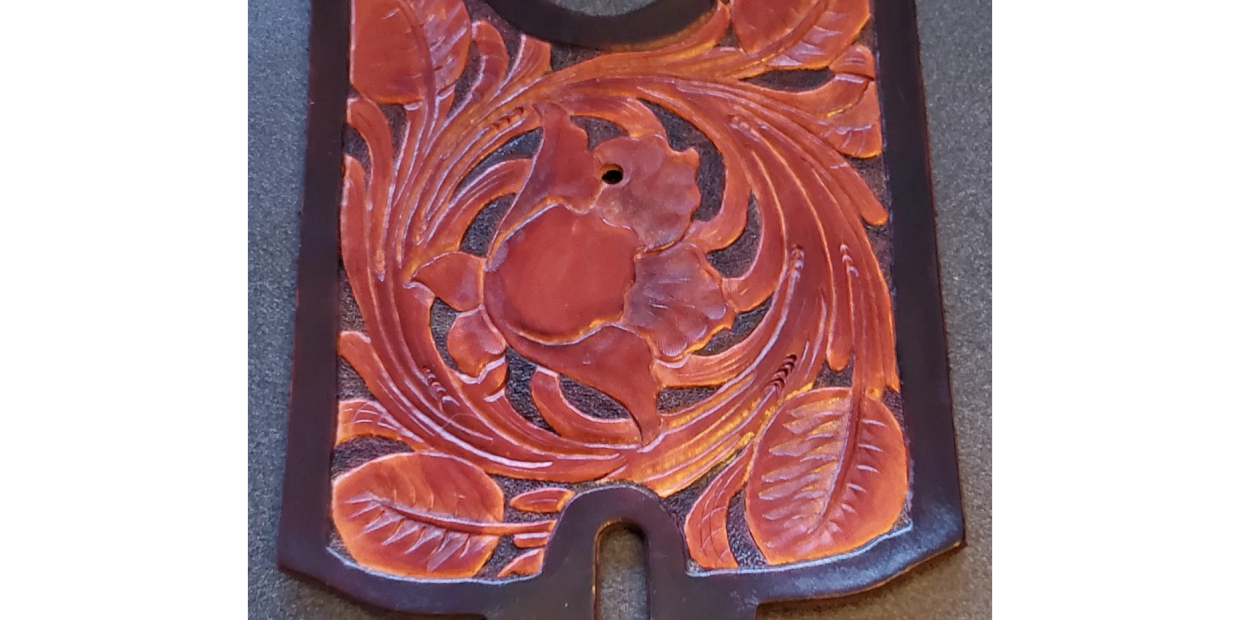 Intricately carved leather piece with floral and leaf patterns.
