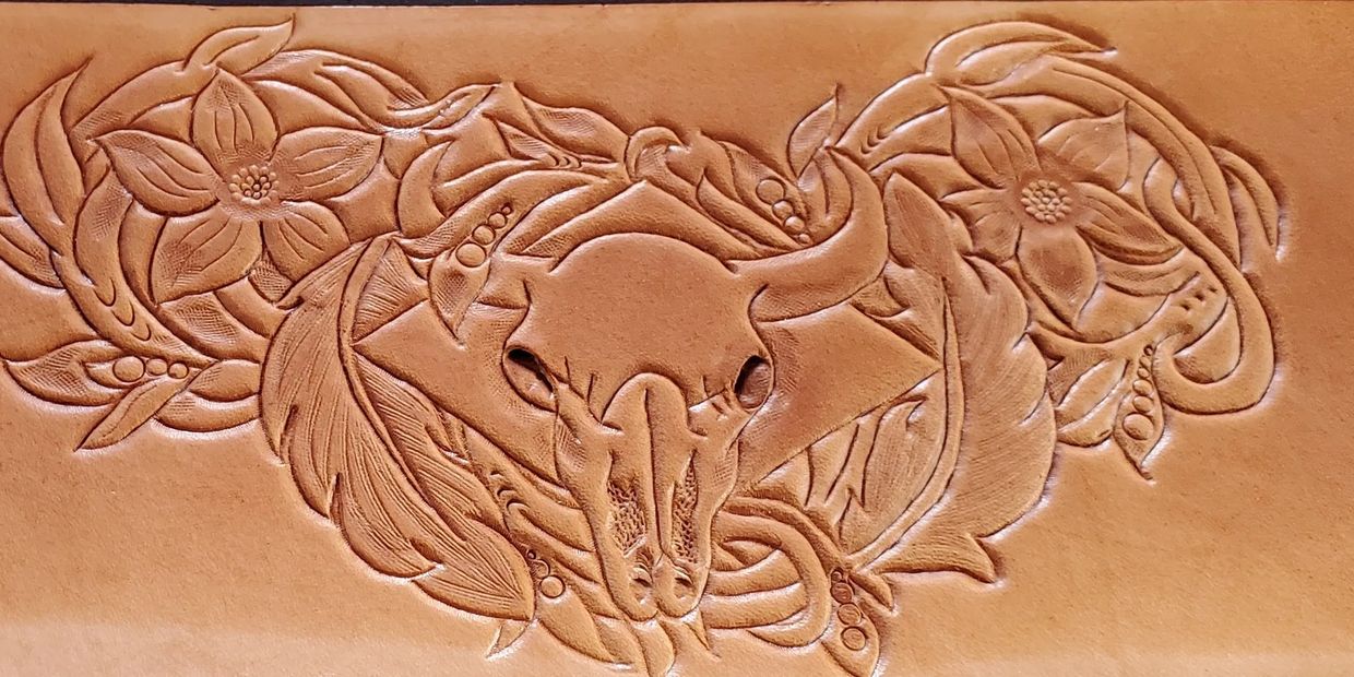Intricate leather carving of a bull skull surrounded by flowers and leaves.