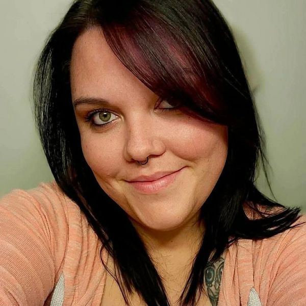 Woman with dark hair and septum piercing smiling at the camera.