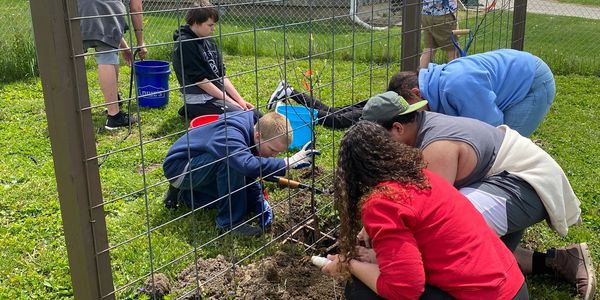 Group of people gardening together near a wire fence.