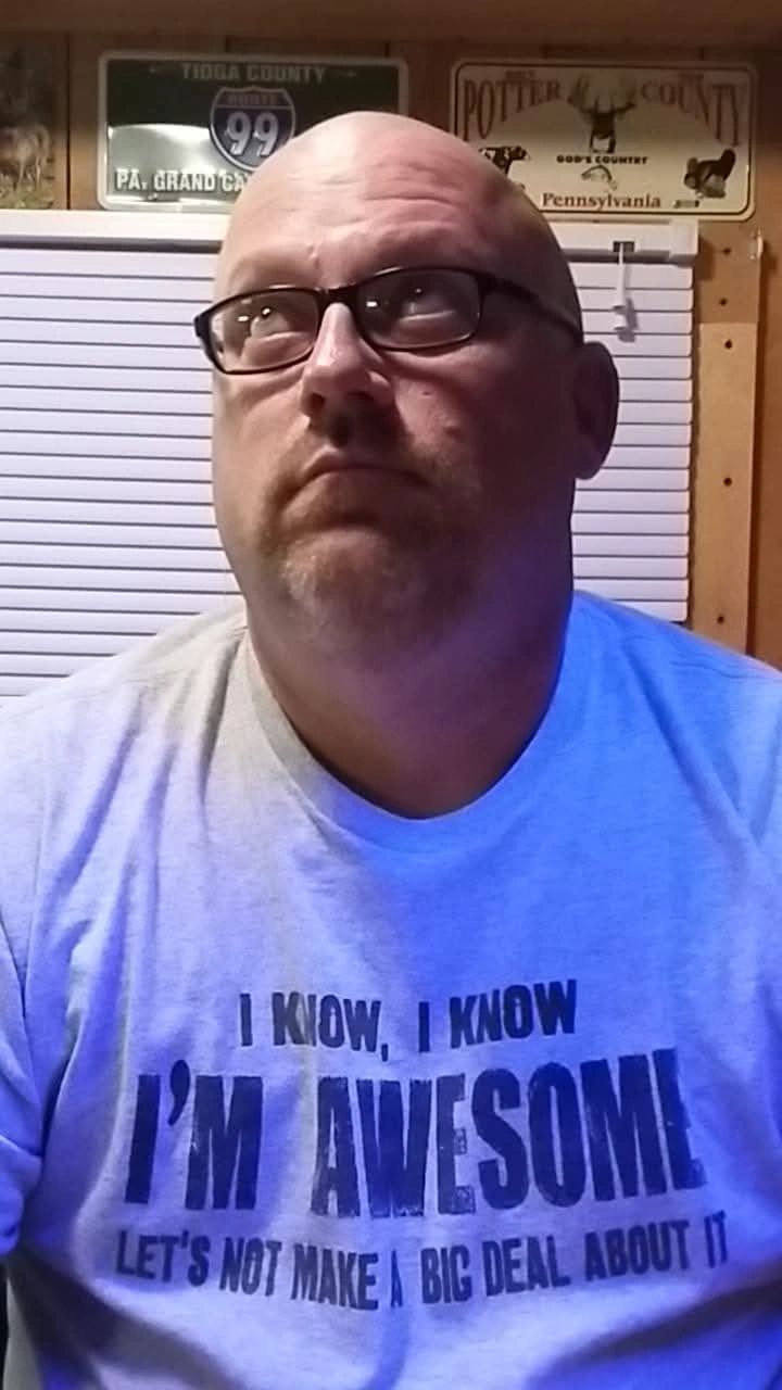 Man in glasses wearing a humorous T-shirt indoors.
