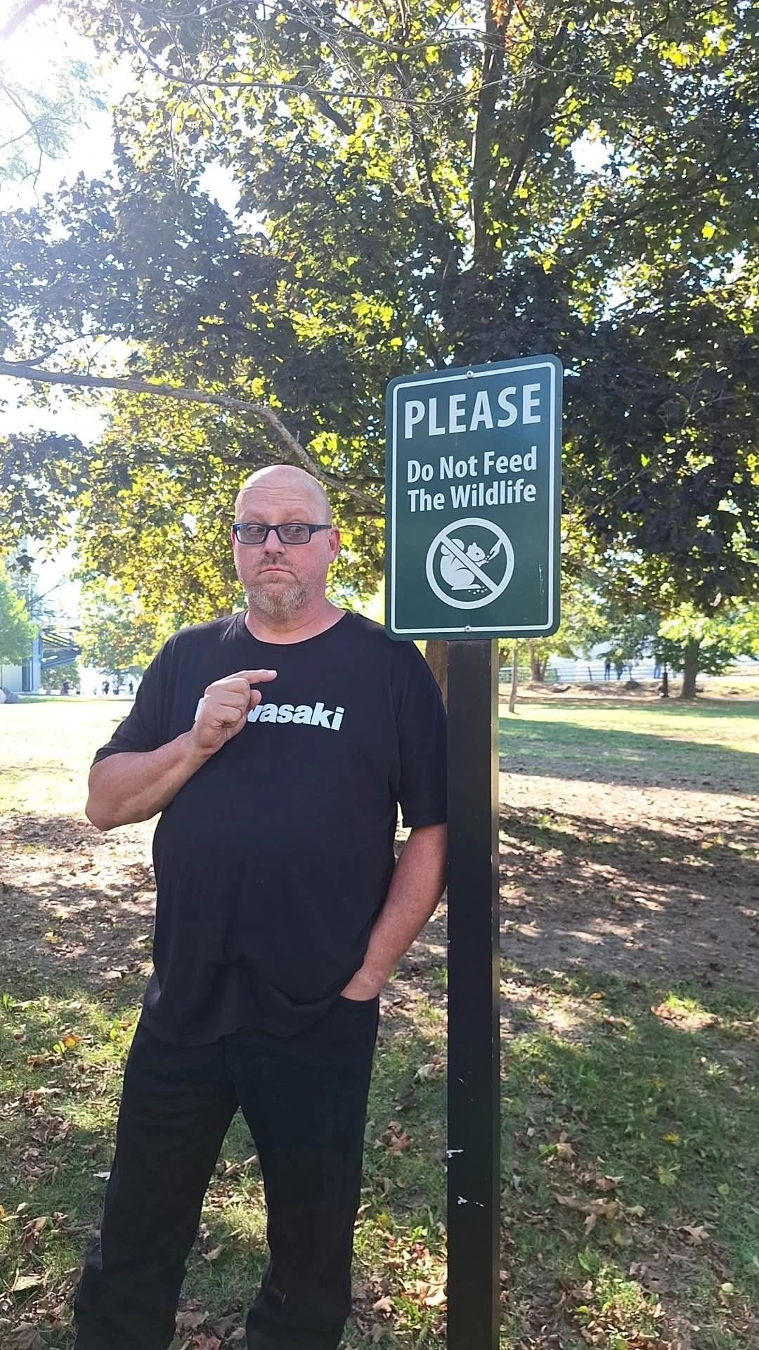Man standing next to a sign that says "Please Do Not Feed The Wildlife."