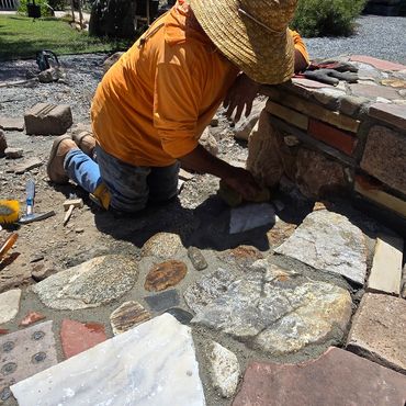 Person laying stones in a detailed outdoor stone wall and floor project.
