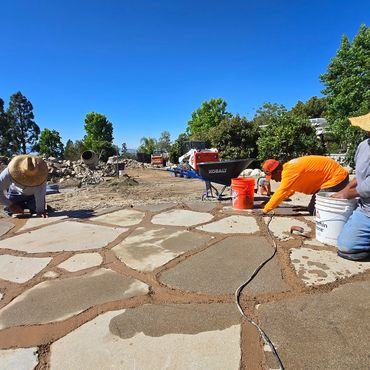 Workers laying stone pavers on a sunny construction site.