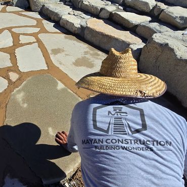 Worker in a straw hat laying stone pavement outdoors.