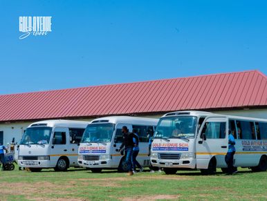 Three white buses parked near a building with people around.