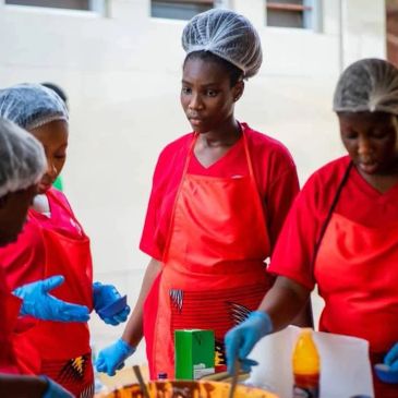 Women wearing red aprons and hairnets working together with food.