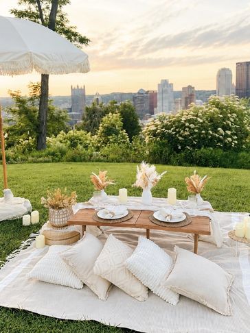 Elegant outdoor picnic setup with pillows and city view at sunset.