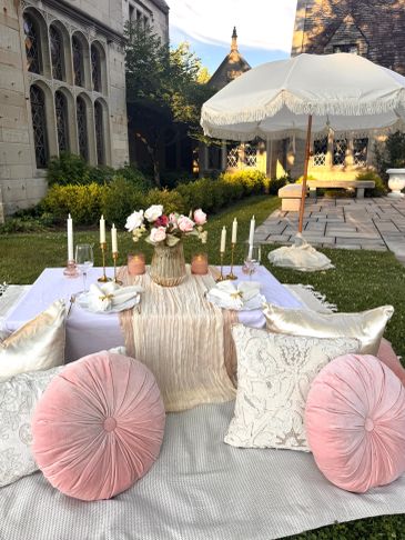 Elegant outdoor picnic setup with pink and white cushions and floral centerpiece.