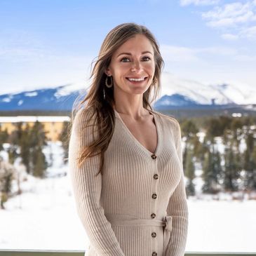 Smiling woman in beige sweater with snowy mountain background.