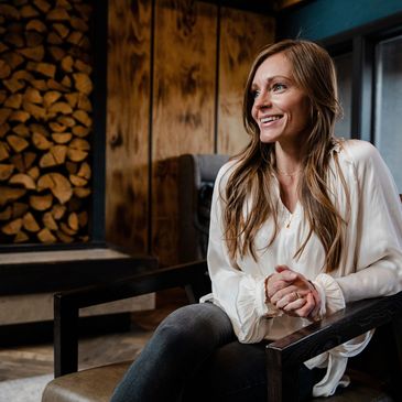 Smiling woman sitting comfortably in a cozy, wood-paneled room.