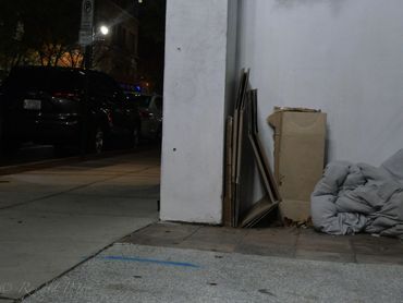 Cardboard and a blanket on a city sidewalk at night.