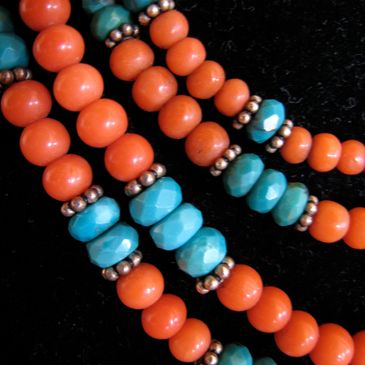 Close-up of turquoise and coral beads with silver spacers on black background.
