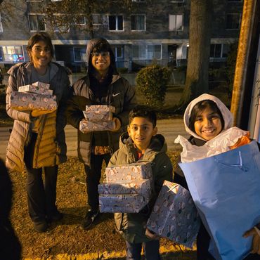 Four kids smiling and holding Christmas presents outdoors at night.
