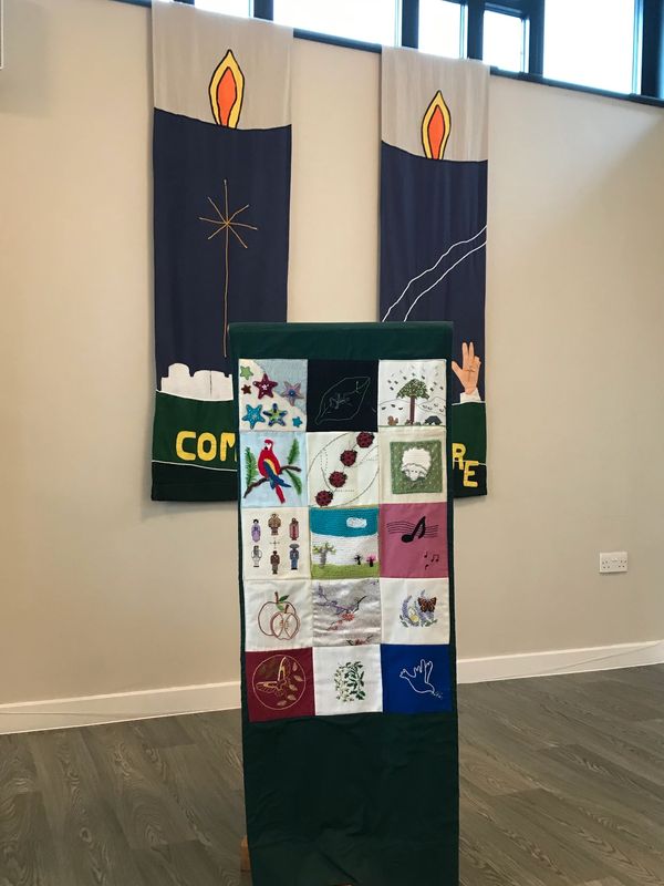 A lectern with a patchwork cover in front of two modern tapestries. 