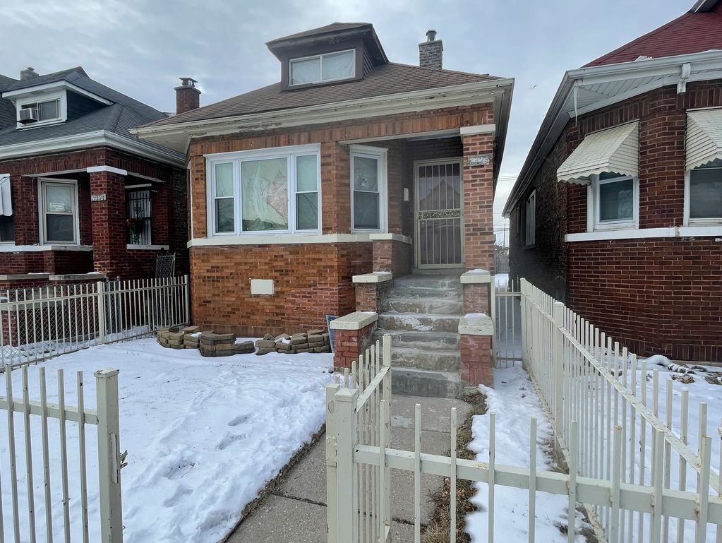 A brick house with snow-covered yard and metal fence on a cloudy day.