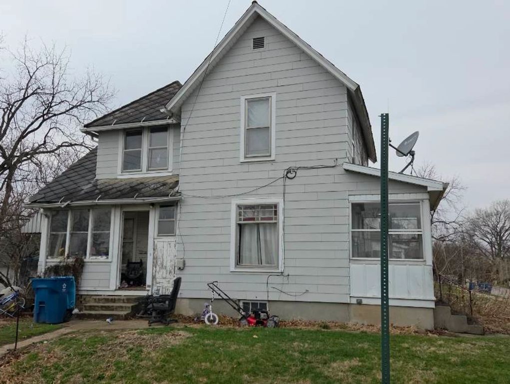 Old gray house with a lawn and some outdoor items scattered around.