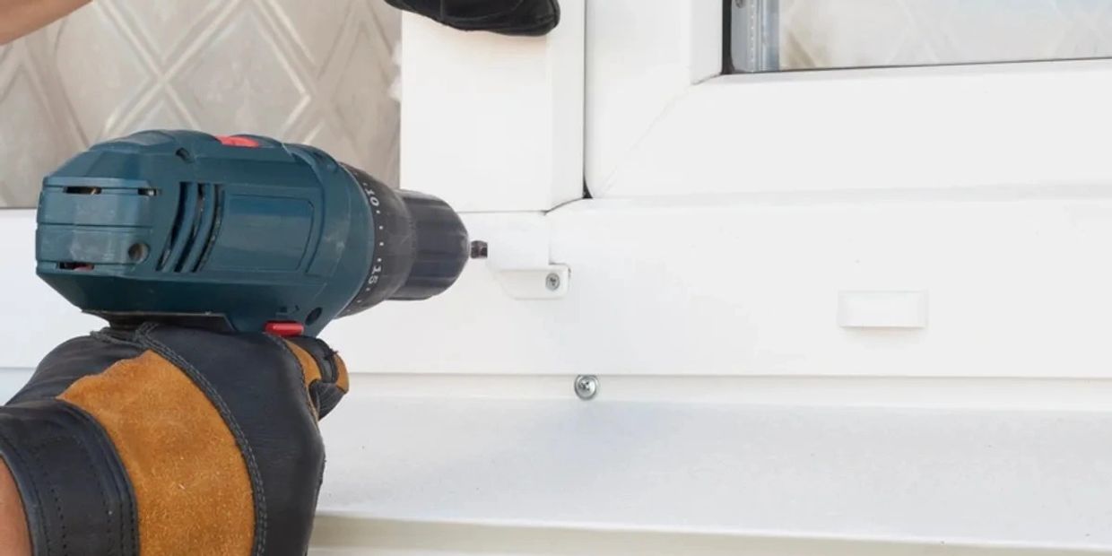 Hand with glove using a cordless drill on a white window frame.