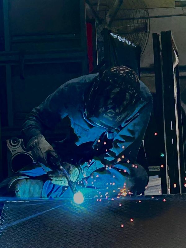 A welder works with bright blue sparks illuminating the scene.