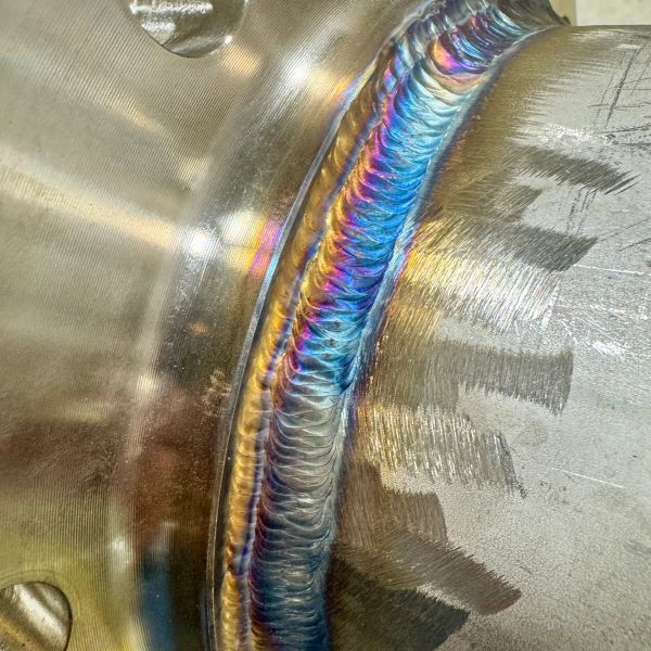 Close-up of a colorful, precise weld on metal with iridescent hues.