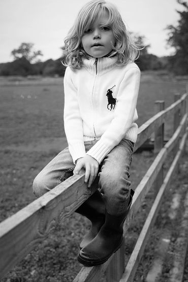 Young child with long hair sitting on a wooden fence outdoors.