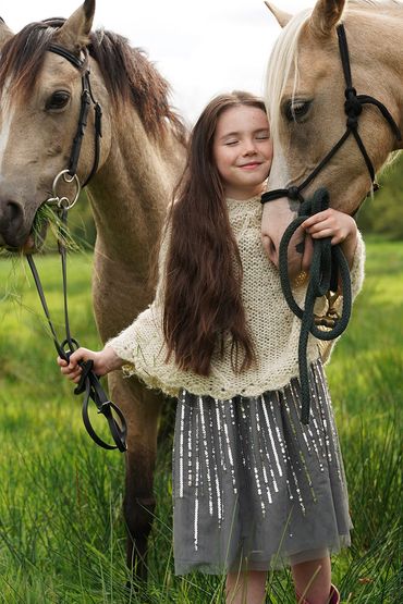 A girl happily hugging two horses in a green field.