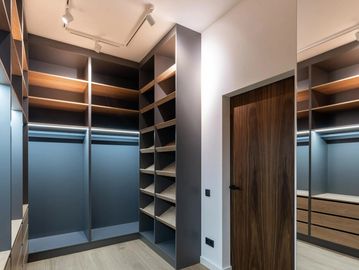 Modern empty walk-in closet with dark shelves and wooden door.