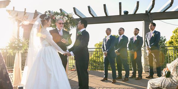 Bride and groom exchange vows outdoors with groomsmen standing by at sunset.