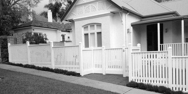 White picket fence surrounding a traditional house with a front porch.