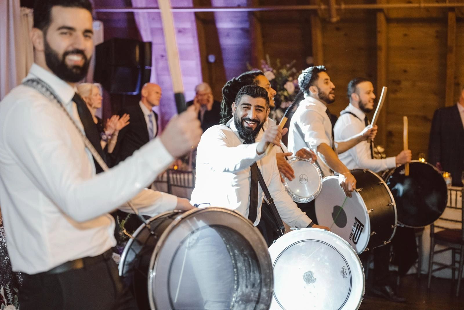 Group of men playing drums joyfully at an indoor event.