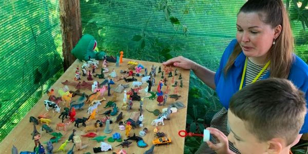 Woman and boy interacting with toy animals on a table outdoors.