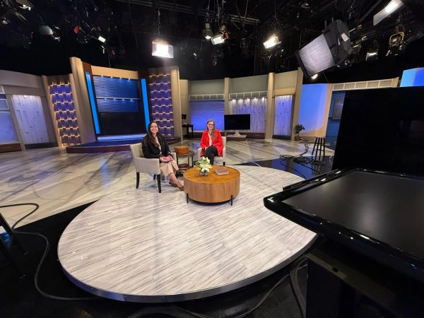 Two women seated on a TV show set with cameras and monitors.