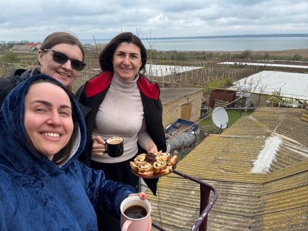Three women enjoying coffee and pastries outdoors with a scenic background.