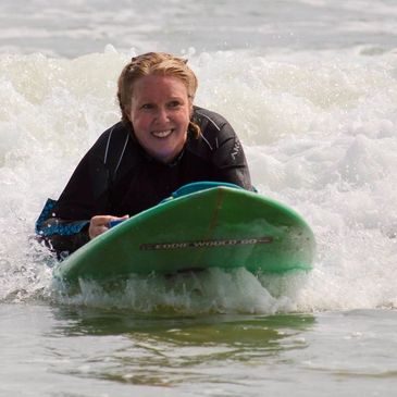 woman laying surfboard smiling as she rides in to shore on a small wave