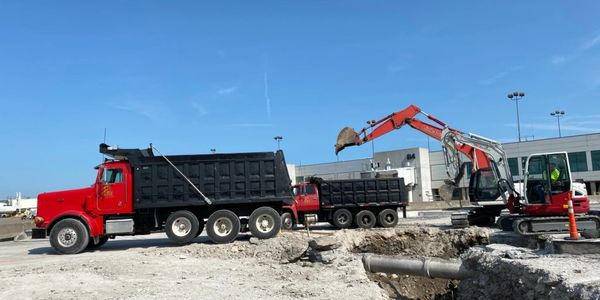 Greenway excavator loading a dump truck with a team of underground utilities contractors