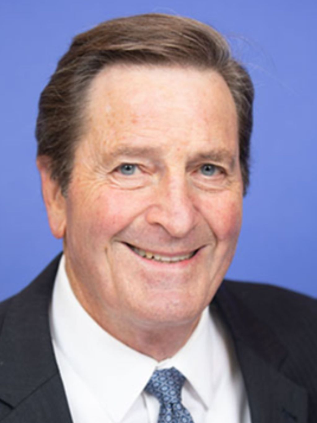 Smiling elderly man in suit and tie against blue background.
