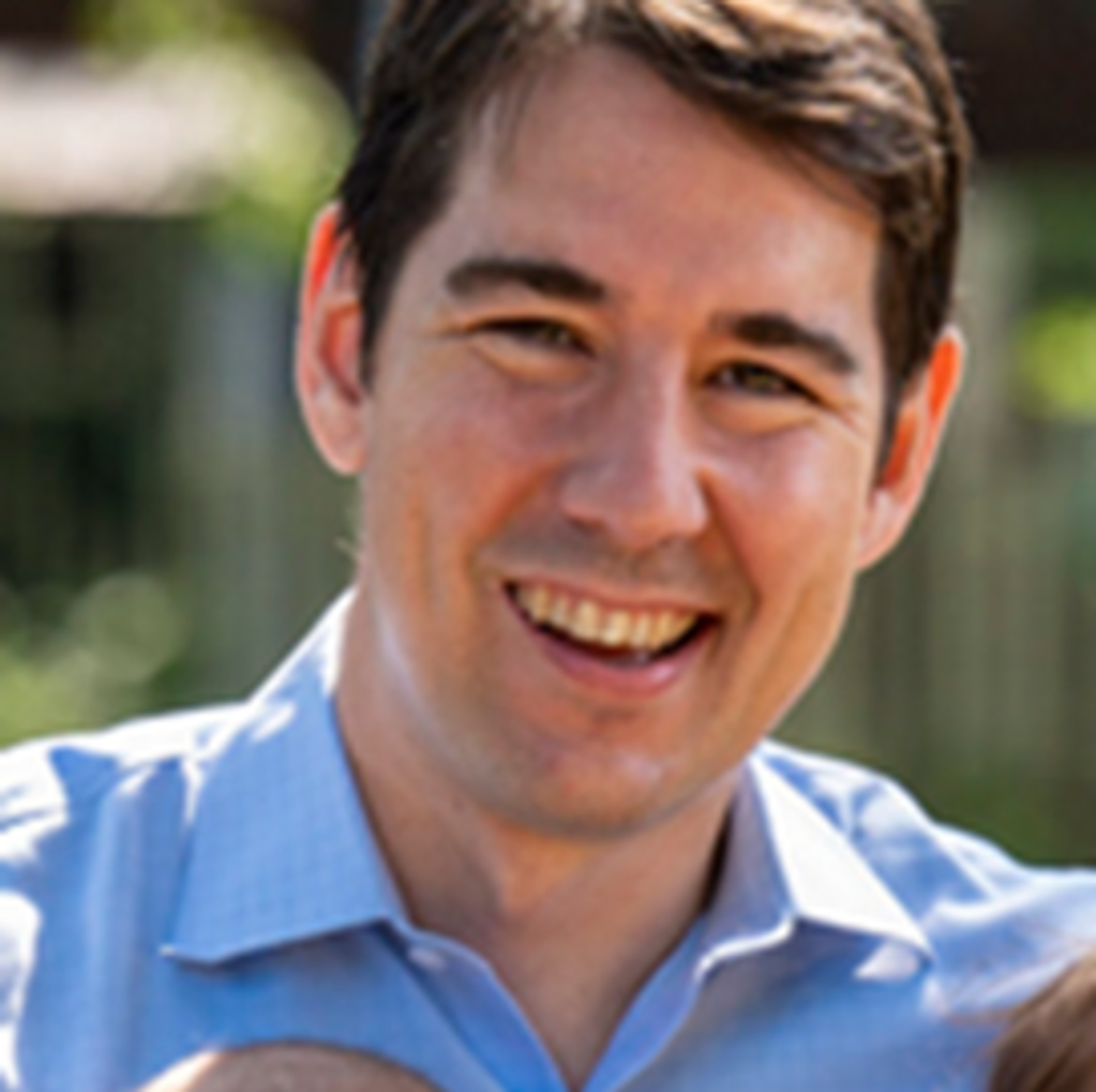 Smiling man in blue shirt outdoors on a sunny day.