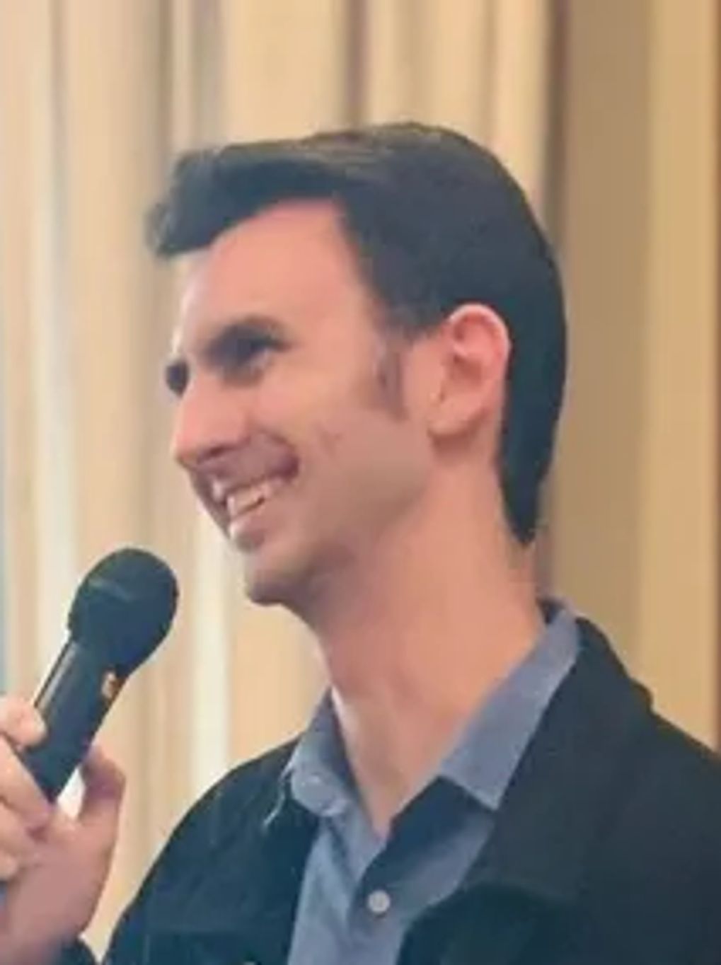 Man smiling and speaking into a microphone indoors.