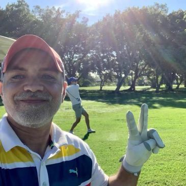 Hombre sonriente haciendo señal de paz en campo de golf.