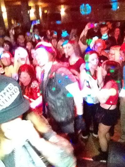 Crowded party scene with people dancing and colorful lights.