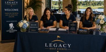 Four women welcome guests at Legacy Golf Events registration desk.