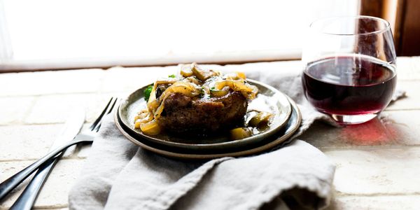 a place setting with linen, plate with steak, a tumbler with a glass of red wine, nife & fork